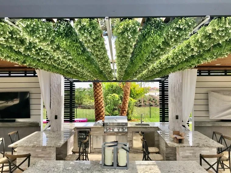Outdoor kitchen with a granite island and grill under a planted pergola