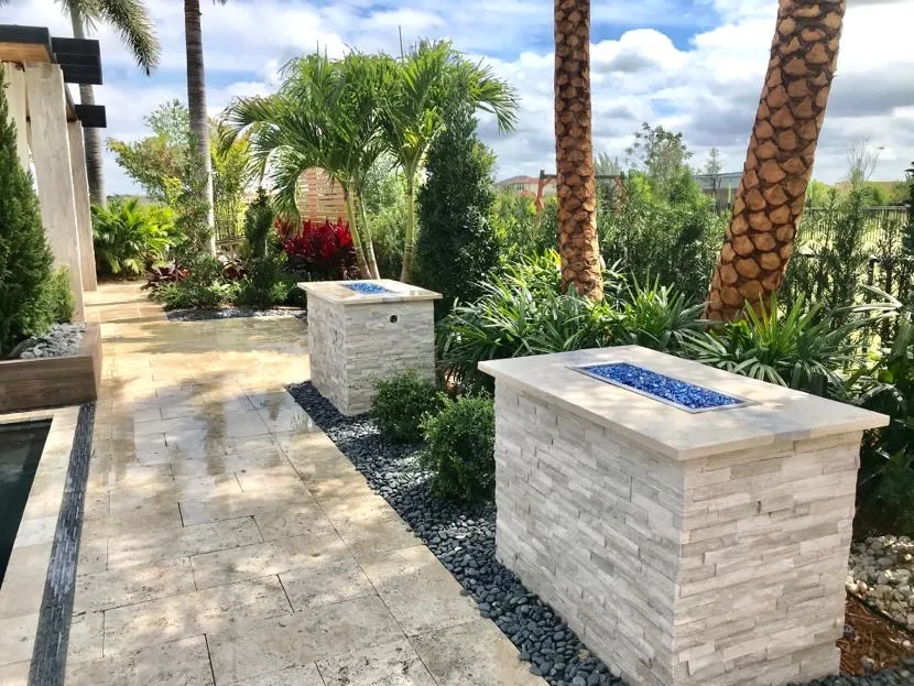 Travertine paver patio with stacked-stone fire tables and tropical landscaping