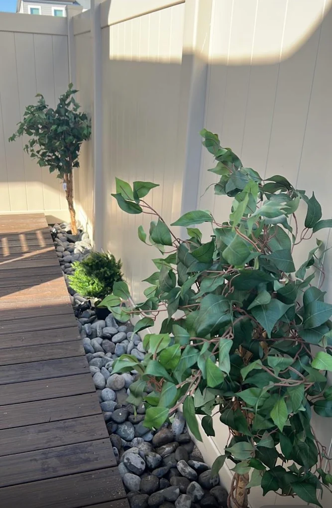 Cream vinyl privacy fence beside a composite deck with a river-rock border